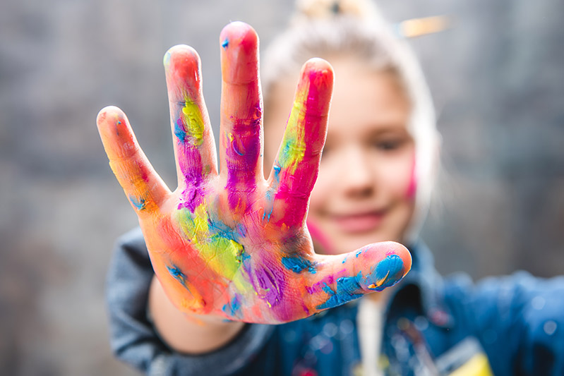 A young girl shows off her paint covered hands. Online resources for children featured image.