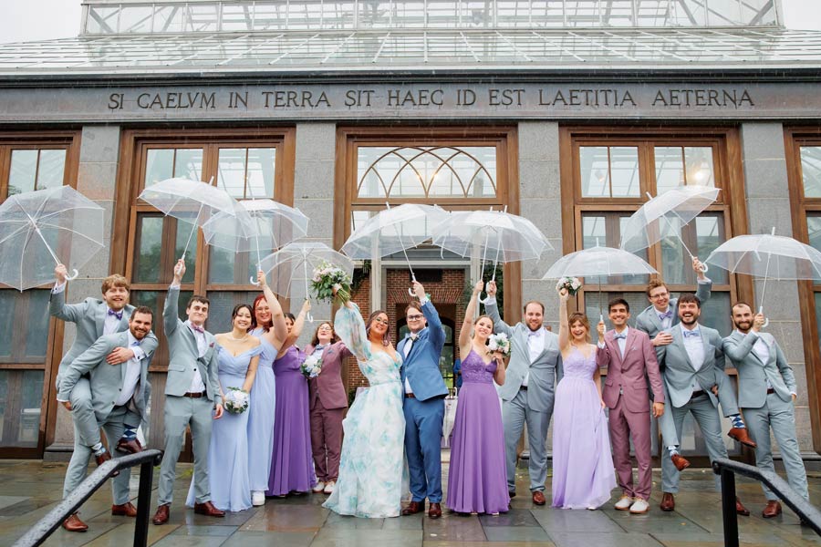 A wedding party poses for a photo holding clear umbrellas in front of the Orangerie.